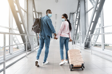 Travels During Coronavirus. Black Couple In Medical Masks Walking In Airport Terminal