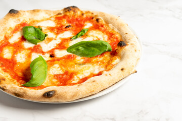 Cropped photo of a baked pizza with buffalo mozzarella, tomatoes sauce and basil. Traditional Italian dish on withe table. Close-up. Copy space, top view. High quality photo