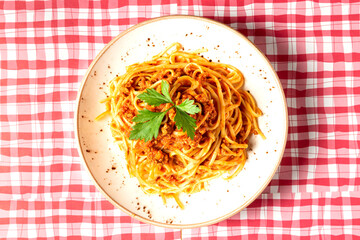 View from above of delicious spaghetti bolognese style dish decorated with a basil leaf on a red and white checkered tablecloth. Typical Italian cuisine. High quality photo
