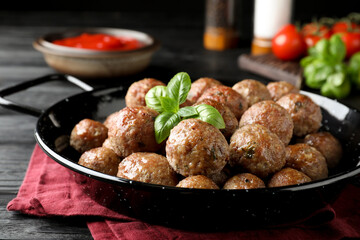 Tasty cooked meatballs with basil on black wooden table, closeup