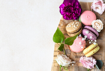 Various types of colorful macarons or macaroons decorated with flowers on light background. Traditional french almond dessert with sweet filling. Top view.