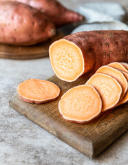 Whole and slices raw sweet potatoes on wooden kitchen board, organic yam. The farm food.