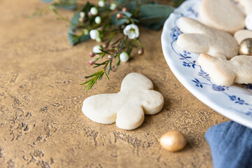 Easter cookies on a ceramic plate with floral decor and candies shaped eggs, stone background. Homemade butter and sugar cookies. Holiday concept.