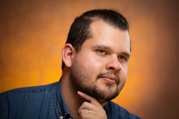 Obraz premium Studio portrait of a young latin man, he poses while looking away thinking with a hand under his chin