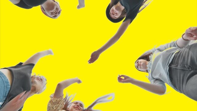 Cheerful female friends join hands on a yellow background as a sign of strong friendship.