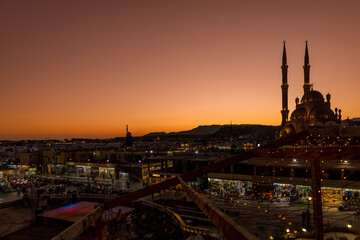 Panoramic top view of Al Sahab mosque and old town at sunset. Silhouettes of people in shopping area with souvenirs in shine of night lights, Sharm El Sheikh, Egypt. High quality photo