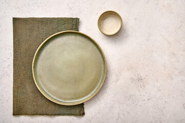 Blank green plate with napkin and saucepan on white textured background. Design concept, copy space