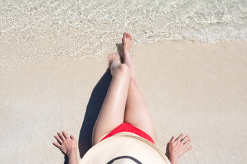 Woman in hat sitting on sand in tropical beach in Thailand.