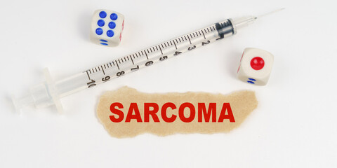 On a white surface lies a syringe, dice and a piece of paper with the inscription - SARCOMA