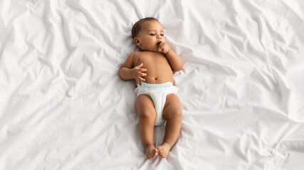 Cute little African American baby lying on bed at home