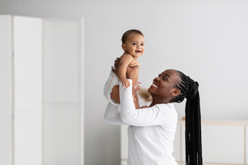 Black woman playing with her cute little baby at home - obrazy, fototapety, plakaty