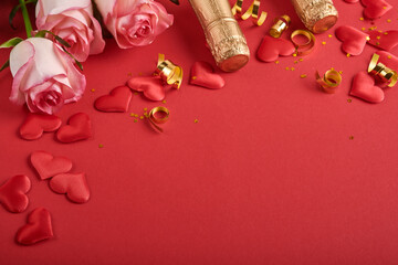 Pink roses flowers, champagne, gift, golden ribbons and confetti red hearts on red background. Top view flat lay with space for your greetings. Valentines day background and greeting card.