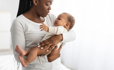 Black mother holding crying baby with colic on hands