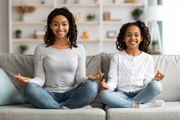 Cheerful black mother and daughter sitting on couch, meditating