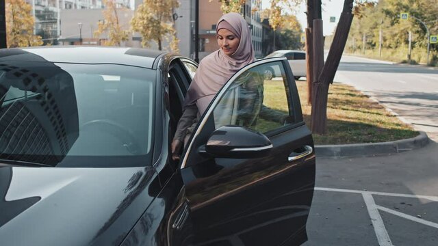 Muslim Woman In Hijab And Casual Outfit Walking On Parking, Getting In Car And Sitting On Driver Seat