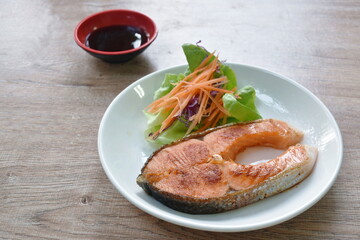grilled salmon steak dipping teriyaki sauce with fresh vegetable salad on plate