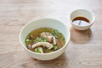 boiled slice pork stomach and bone soup in bowl dipping spicy sauce cup on table