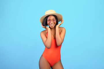 Portrait of carefree black woman in bikini, sunglasses and straw hat posing and smiling at camera...