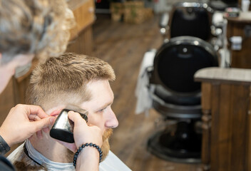 Close up view of the bearded man in barbershop taking care of his beard. Side view of handsome bearded man having his beard cut by hairdresser at the barbershop