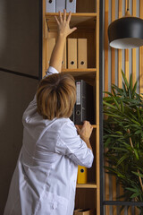 A female doctor pulls a cardboard folder from the shelf.