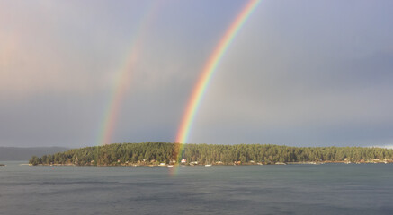 Double Rainbow in the cloudy sky over the pacific ocean and Gulf Islands in Background. West Coast in Vancouver Island, British Columbia, Canada. Nature Background