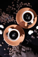 Ceramic coffee cups and beans on an old kitchen table. Dark and white chocolate candies. Top view.