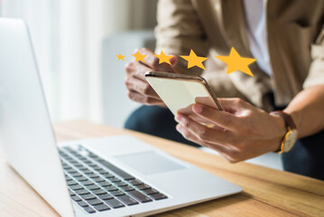 Young man pressing face emoticon on the smart phone and selecting icon 5 star rating. Demonstrates that customer satisfaction is essential to a successful business.