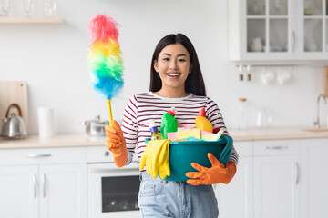 Happy asian lady with cleaning tools standing at kitchen