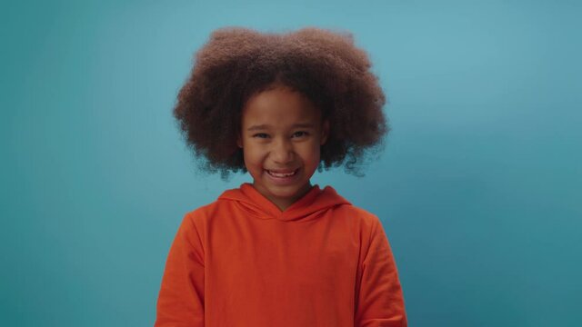 Adorable African American girl showing agreement emotion by shaking her head positively on blue background. Kid says 'yes'.