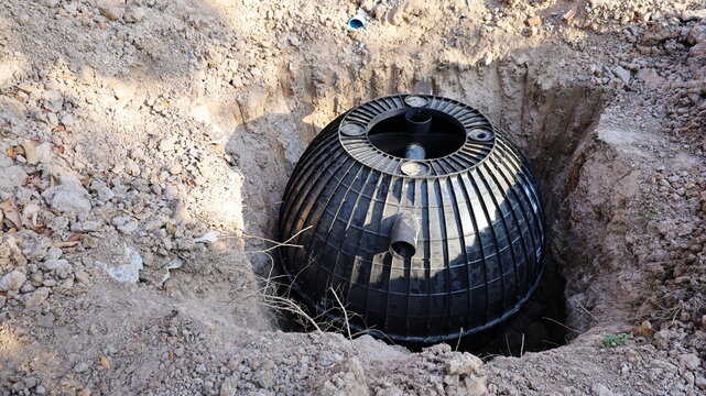 A black septic tank in the pit. Plastic bucket for treating water and waste in an outdoor hole on the ground background in a construction site with copy space. selective focus