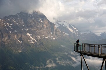 Tourist standing on the edge of the cliff skywalk in First, Grindelwald, opposite the majestic...