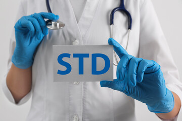 Doctor holding sheet of paper with abbreviation STD on white background, closeup