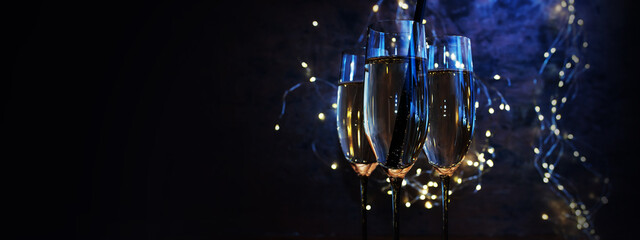 Celebrate with sparkling champagne. Blue illuminated champagne glasses with fairy lights against horizontal black background for new year and party.