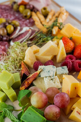 Blurred image of slicing different types of cheese, meat products, micro greens, fruits on the board.