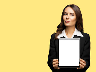 Fototapeta premium Portrait of happy smiling brunette businesswoman showing tablet pc, touchpad, with copy space for text, isolated over yellow colour background. Confident beautiful young business woman at studio