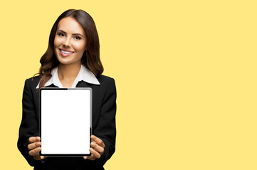 Portrait of happy smiling brunette businesswoman showing tablet pc, touchpad, with copy space area for text, isolated over yellow colour background. Confident attractive business woman at studio