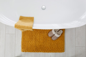 Soft orange bath mat and slippers on floor in bathroom, top view