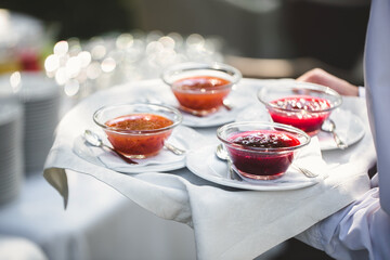 Berry and fruit jam on a tray in the hands of a waiter.