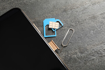 Sim card, mobile phone and ejector tool on grey table, closeup