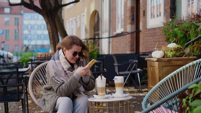 Traveller woman in sunglasses does does photos of her coffe cups by smartphone in the street cafe of old town, 4k 60p slow motion