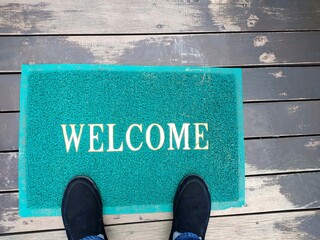 A green welcome doormat with feet wearing black shoes. Interior and object concept. © Aungsumol