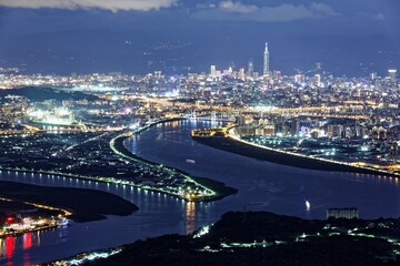 Fototapeta premium Aerial panorama over Taipei, the capital City of Taiwan, on a blue gloomy evening with view of the confluence of Tamsui & Keelung River & Taipei 101 Tower amid highrise skyscrapers in Downtown at dusk