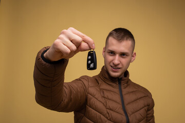 Young 20s man in a brown jacket, on a yellow background, holding in his hand, gives a new car key