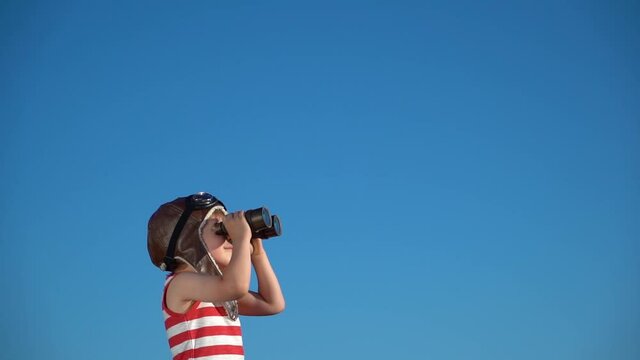 Happy child looking through vintage binoculars against blue sky. Slow motion
