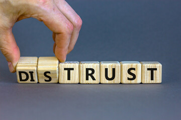 Distrust or trust symbol. Businessman turns wooden cubes, changes words 'distrust' to 'trust'. Beautiful grey table, grey background. Business and distrust or trust concept, copy space.