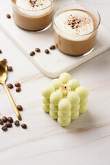 A pale green square bubble candle on a marble kitchen table among coffee beans and sweet dessert - chocolate mouse