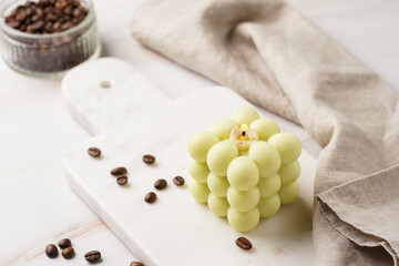 A pale green square bubble candle on a marble kitchen table among coffee beans and sweet dessert - chocolate mouse