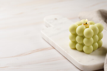 A pale green square bubble candle on a marble kitchen board with off-white linen cloth