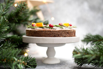 Christmas cake is on the cake stand with candles , tree branches and craft star on the wall.