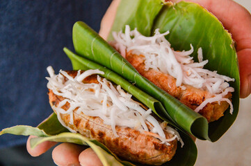 Close up to a tourist foodie's hand holding grilled banana stuffed with young coconut shaving or maak kuai nyad sai which is an authentic traditional vegan streetfood from Laos